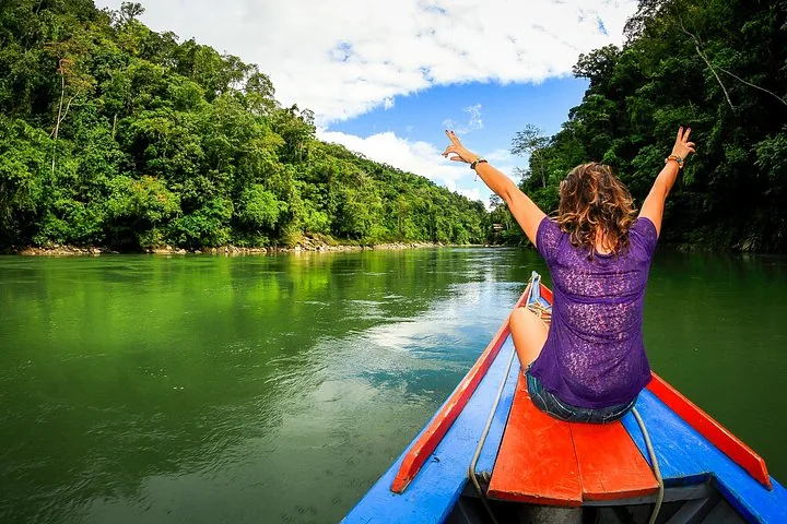 Woman sitting on the bow of a motorized canoe, arms raised, on a river.